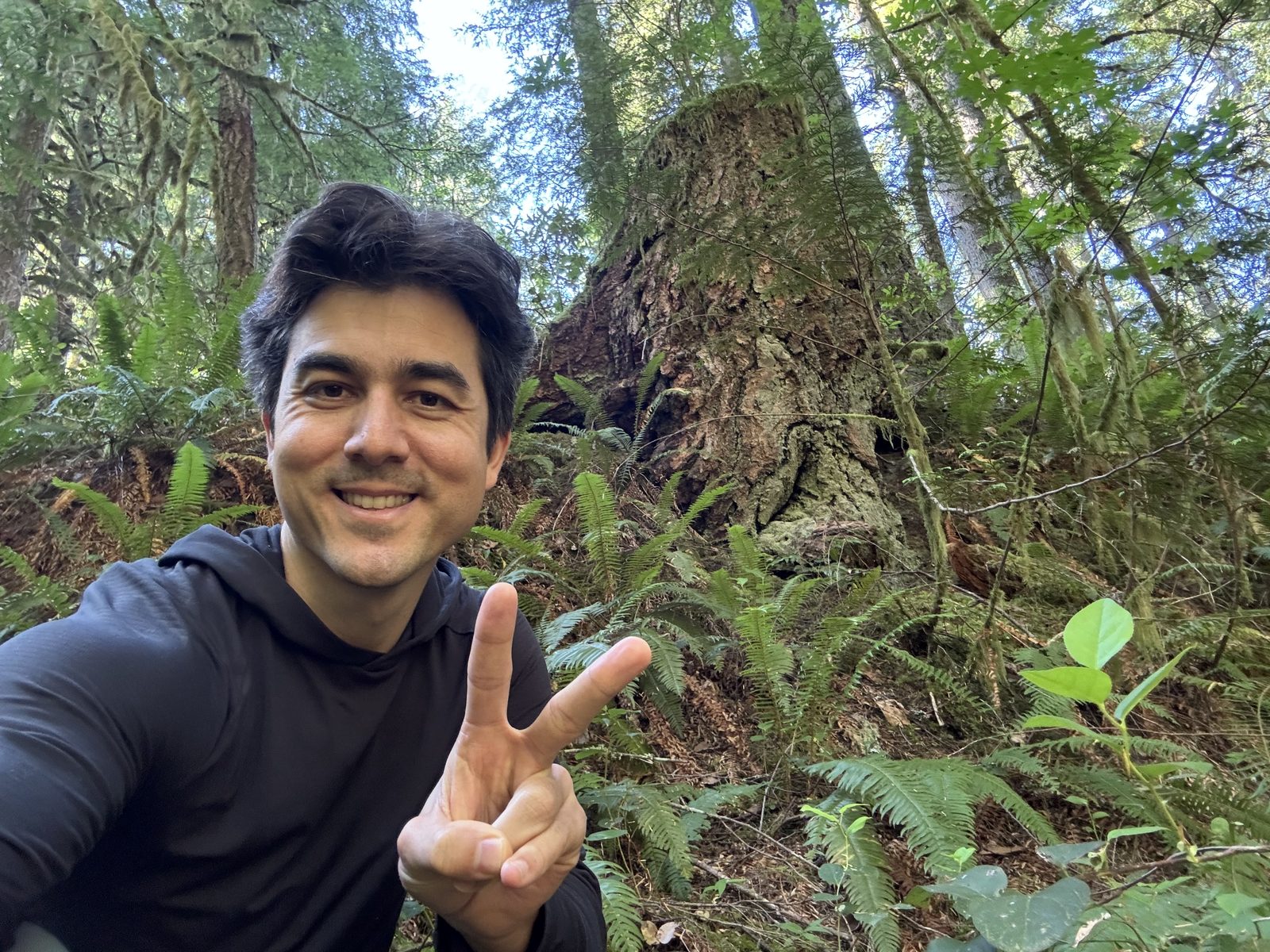 Wes smiling and giving a peace sign in a forest